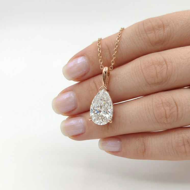 Diamond teardrop pendant on a gold chain held by a hand against a white background