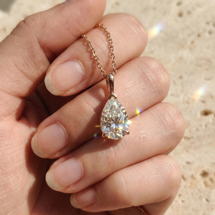 Teardrop-shaped diamond pendant on a chain held in a hand against a neutral background